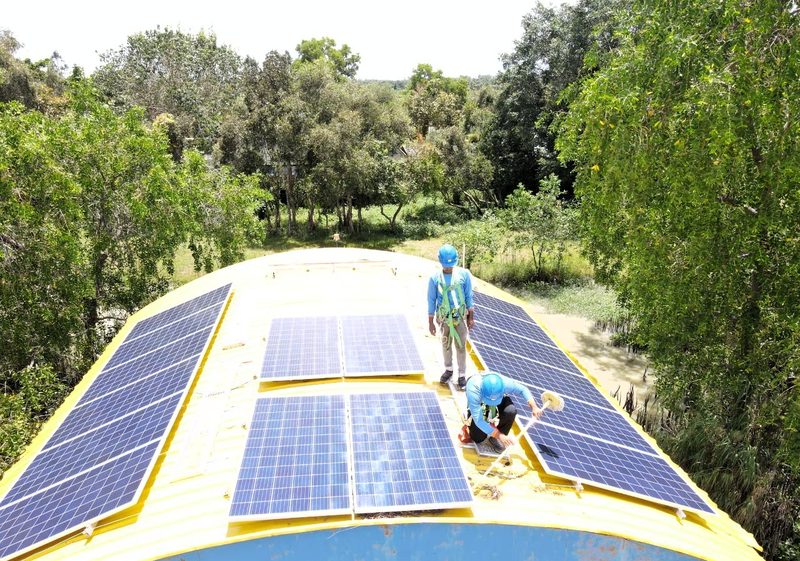 Technician fitting solar panels on the roof of a yellow patrol boat