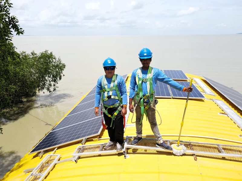 Two technicians standing on the boat roof beside the panels